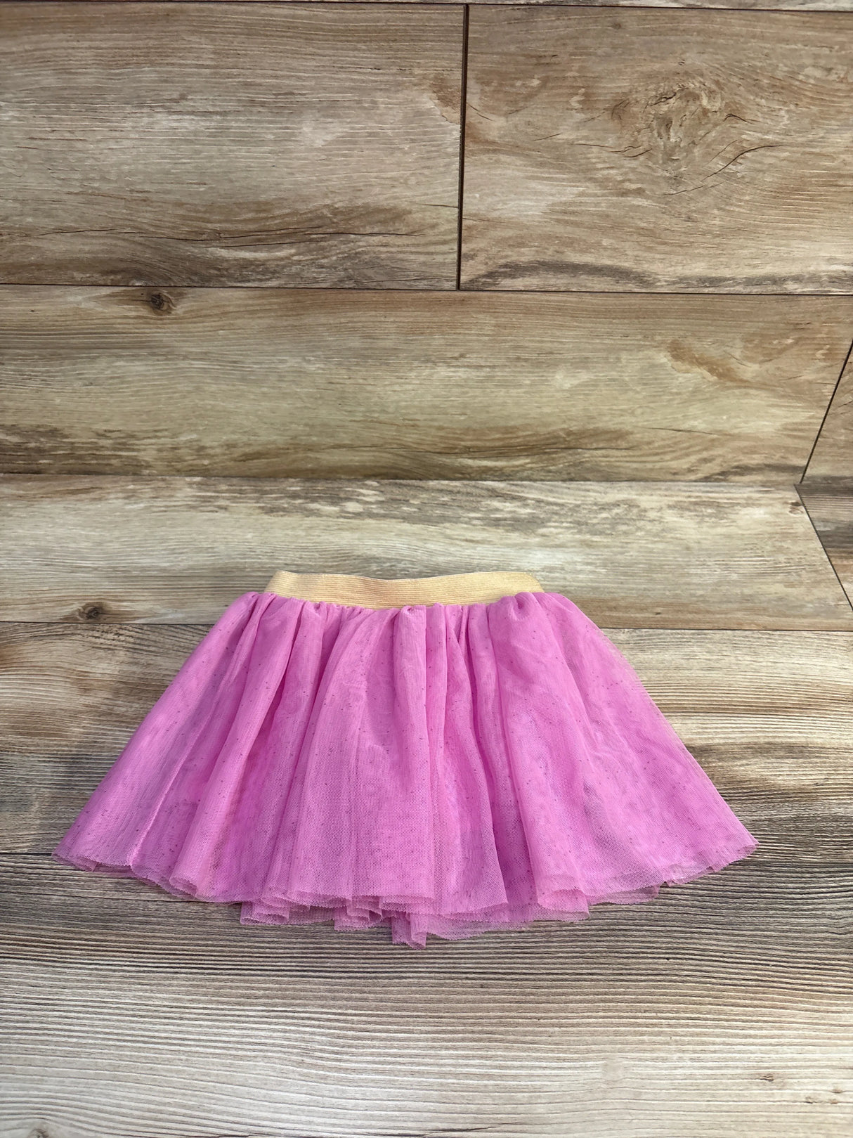 Top-down view of pink layered tulle toddler skirt with gold elastic waistband on light wood background