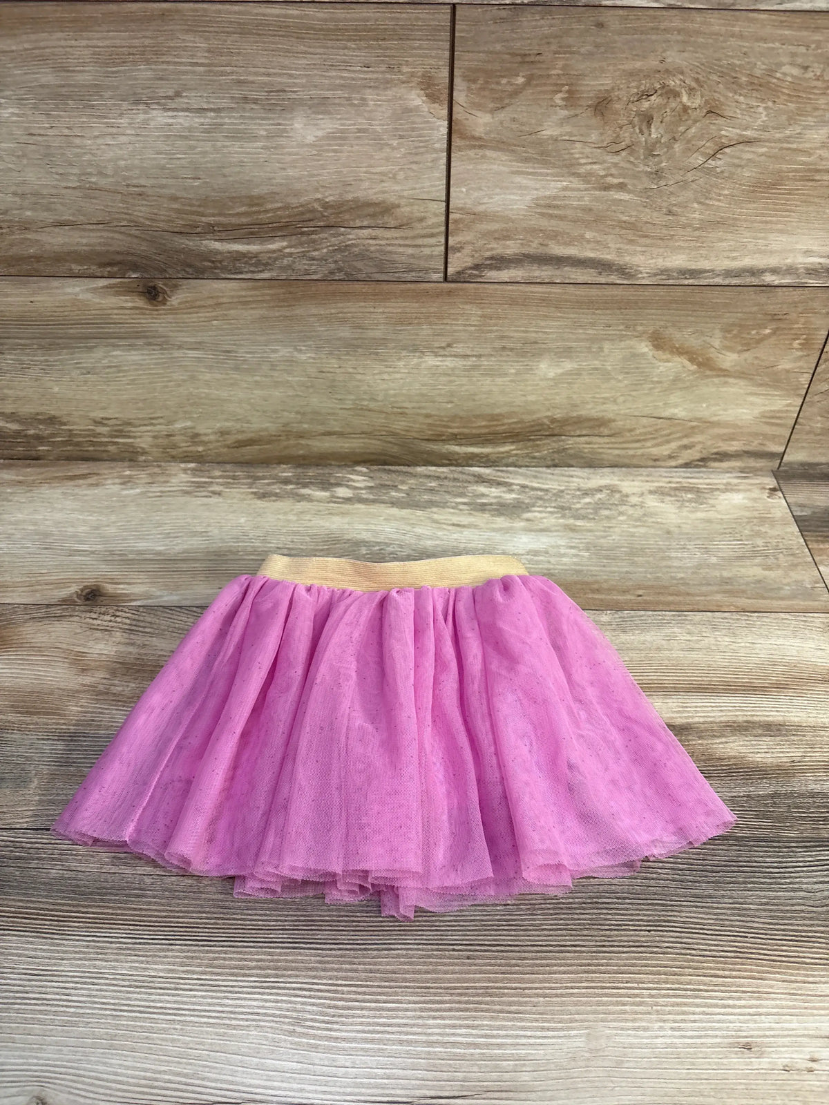 Top-down view of pink layered tulle toddler skirt with gold elastic waistband on light wood background
