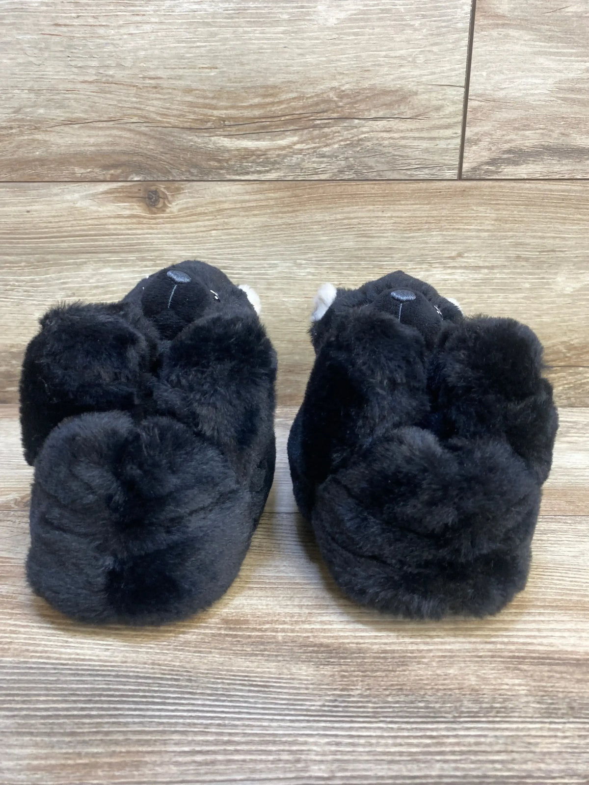 Pair of plush black animal slippers for kids on wood floor