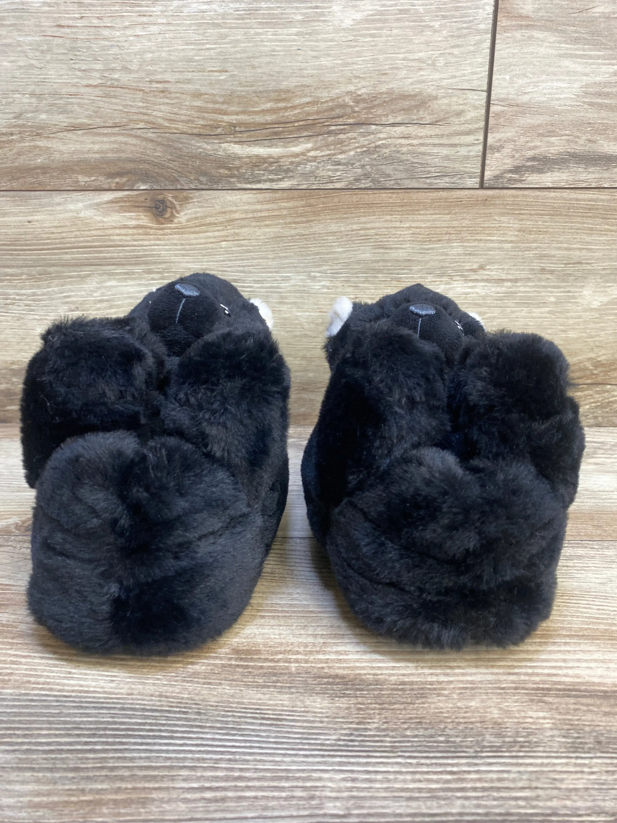 Pair of plush black animal slippers for kids on wood floor