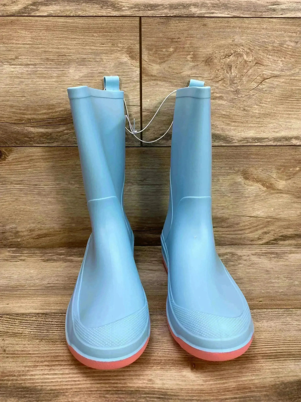 Front view of Cat & Jack Andy slip-on light blue kids’ rain boots with pink soles, pull tabs, textured toe on wood background