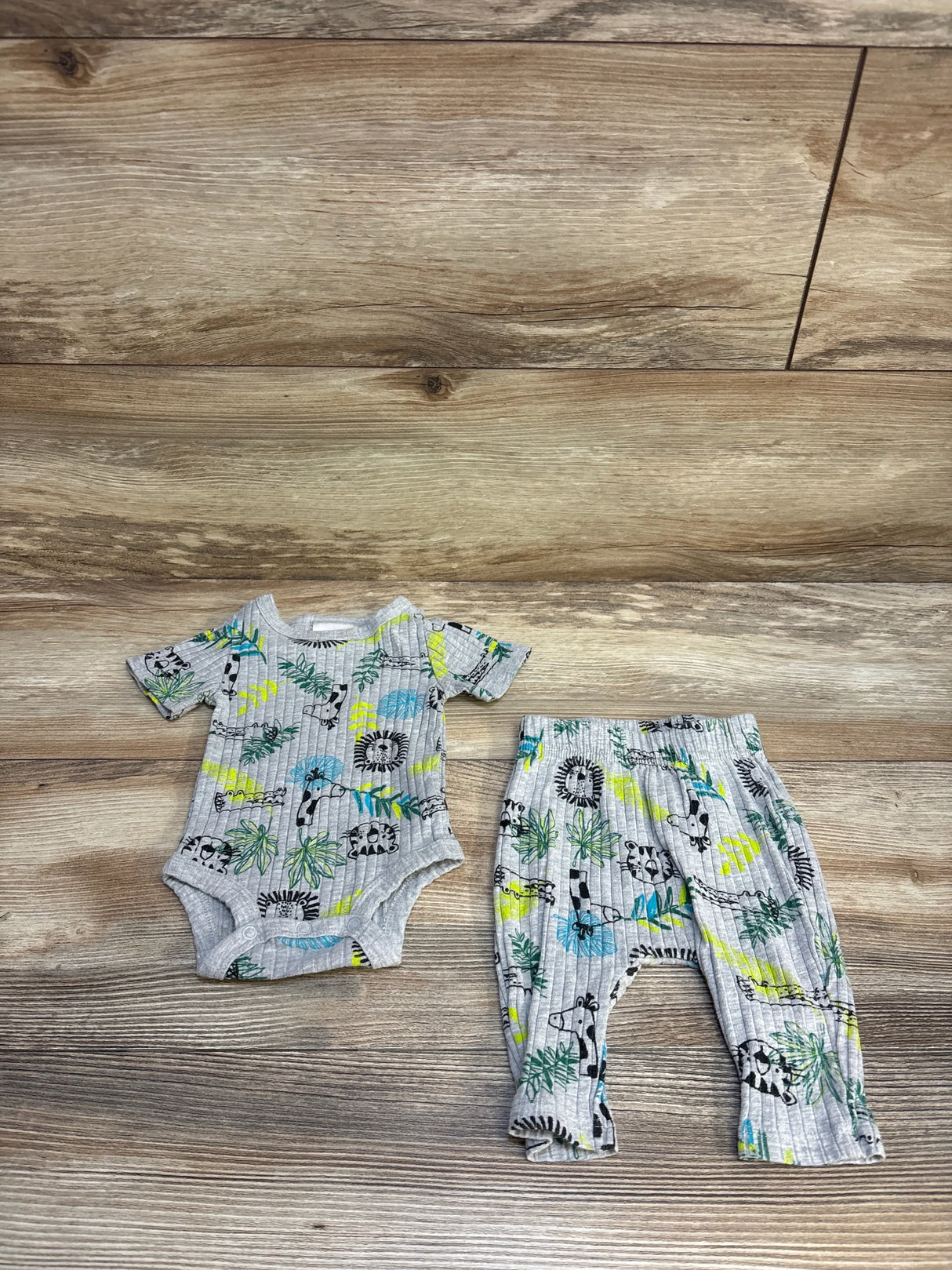 Gray ribbed baby bodysuit and pants set with jungle animal print, laid on wood floor