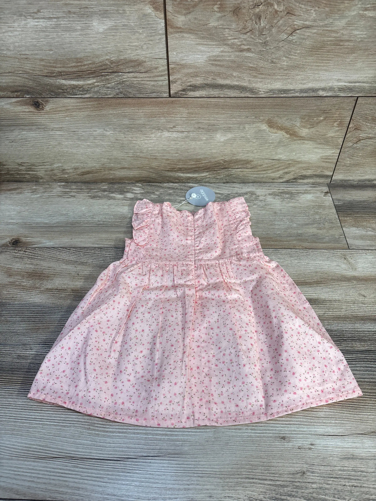 Back view of Wedoble pink floral sleeveless dress showcasing ruffled shoulders and back zipper on a wood-grain background