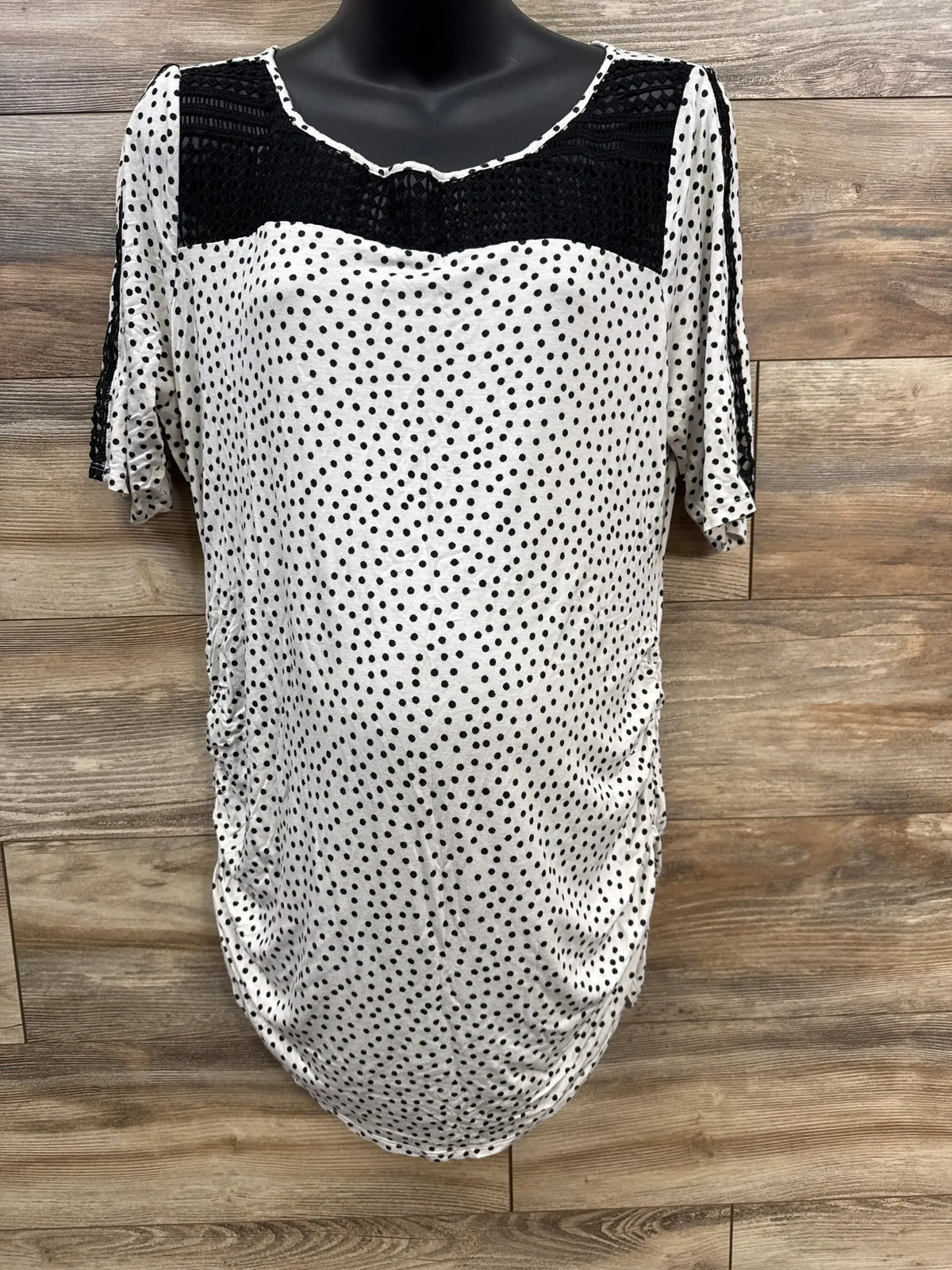 White polka dot maternity top with black crochet detail on wooden background
