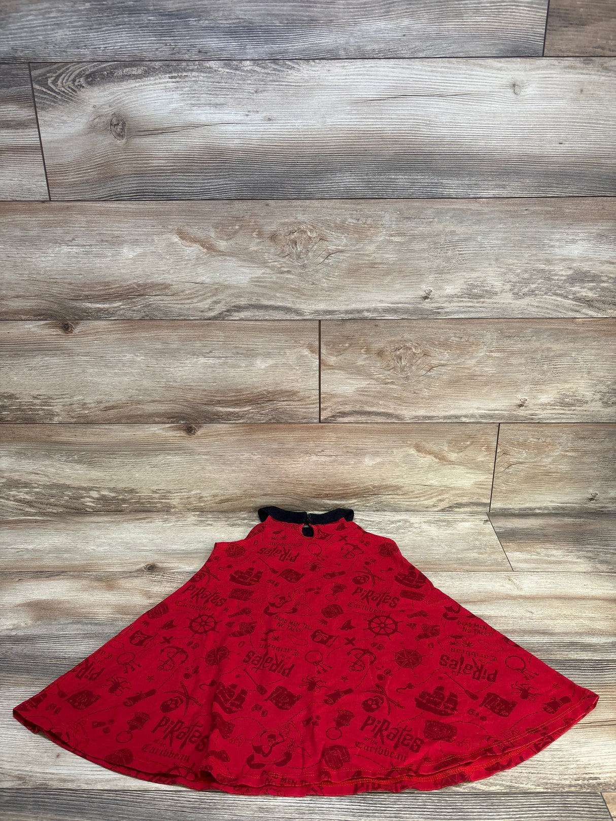 Flat lay of red girls Disney Minnie Mouse Pirates dress with flared skirt and all over pirate print on light wood floor