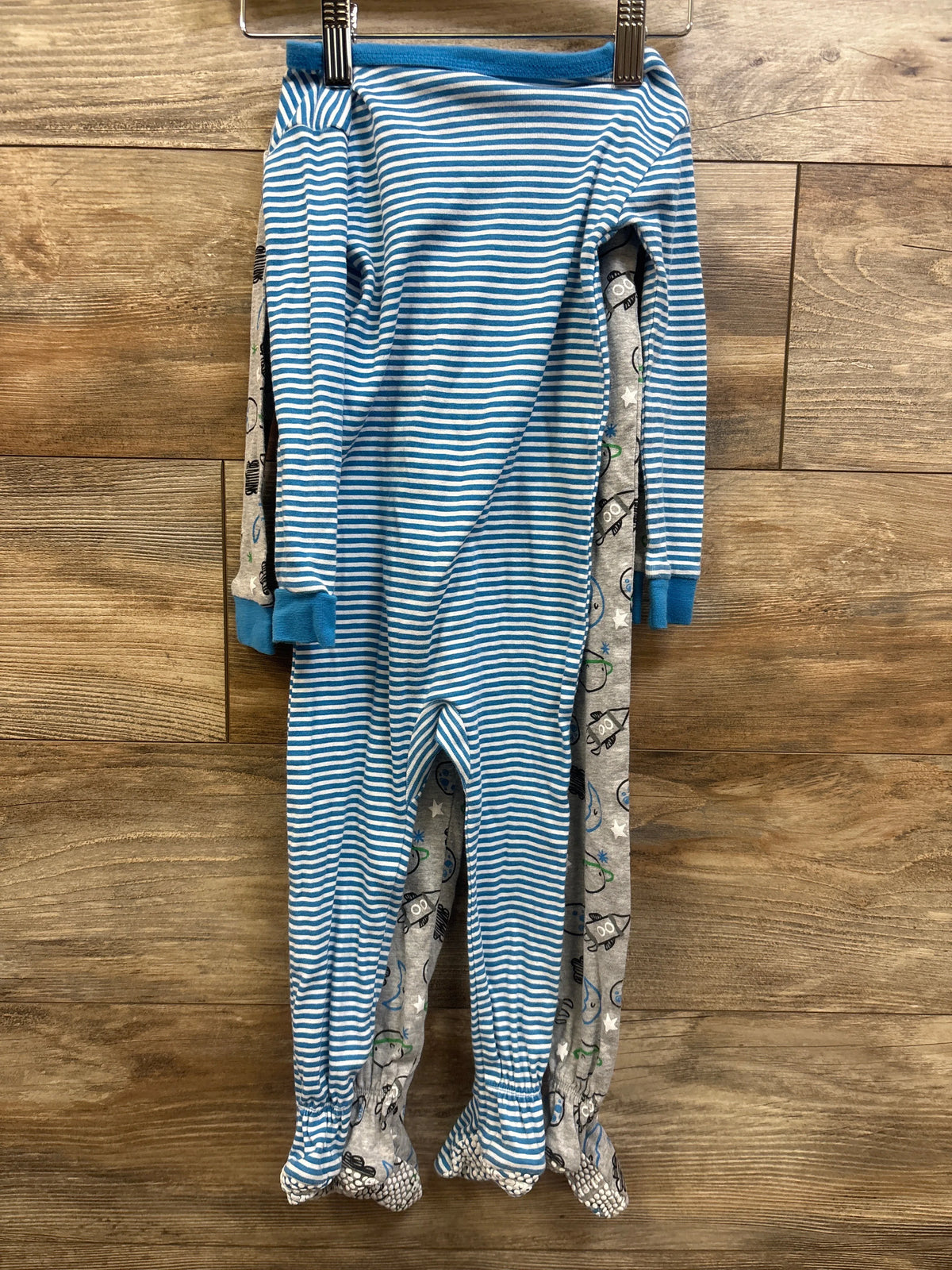 Front view of Gerber 2pk Sleep N Play sleepers in blue and gray patterns size 24m hanging over wood flooring
