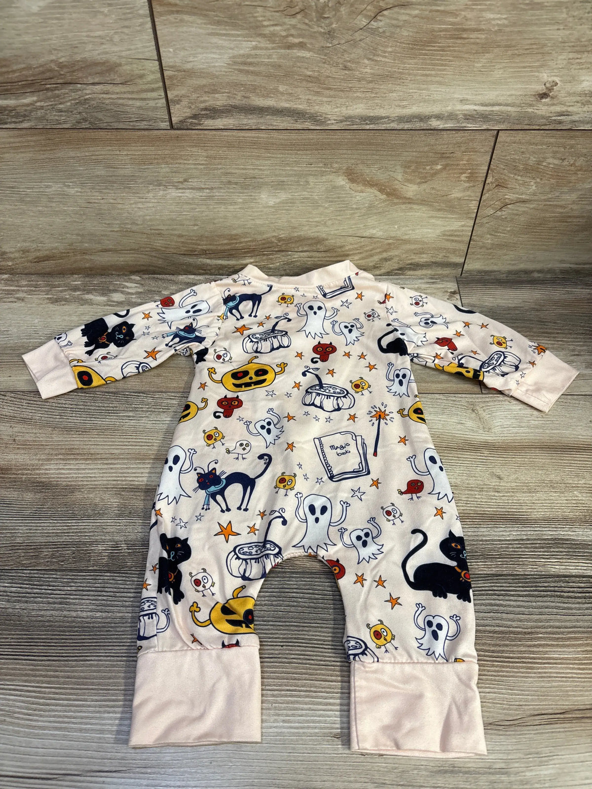 Flat lay of baby Halloween coverall showcasing ghosts, pumpkins and black cats with wood floor background