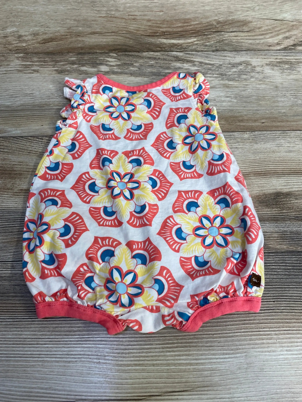 Top view of TEA floral baby romper showing ruffle shoulder and elastic leg openings on wooden floor