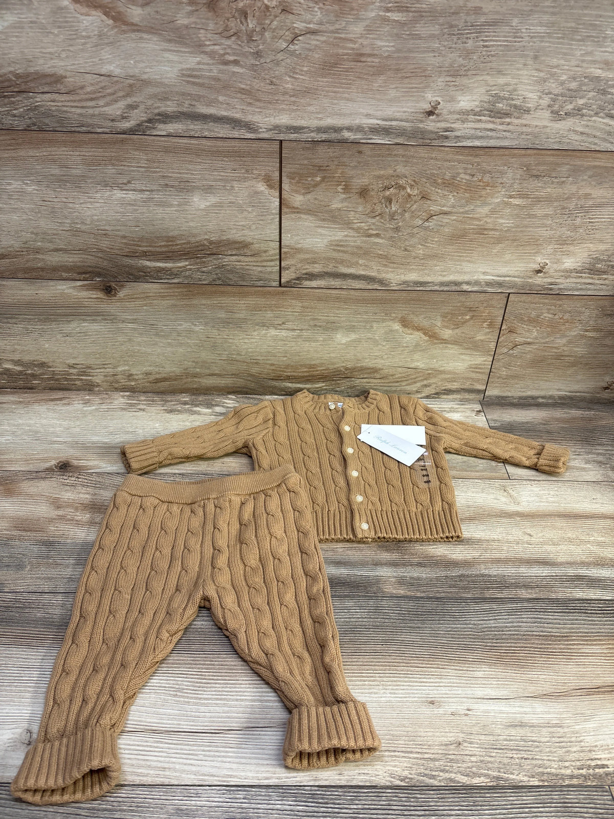 Flat lay of a Ralph Lauren two-piece cable knit cardigan sweater and pants set in tan with a wood plank background