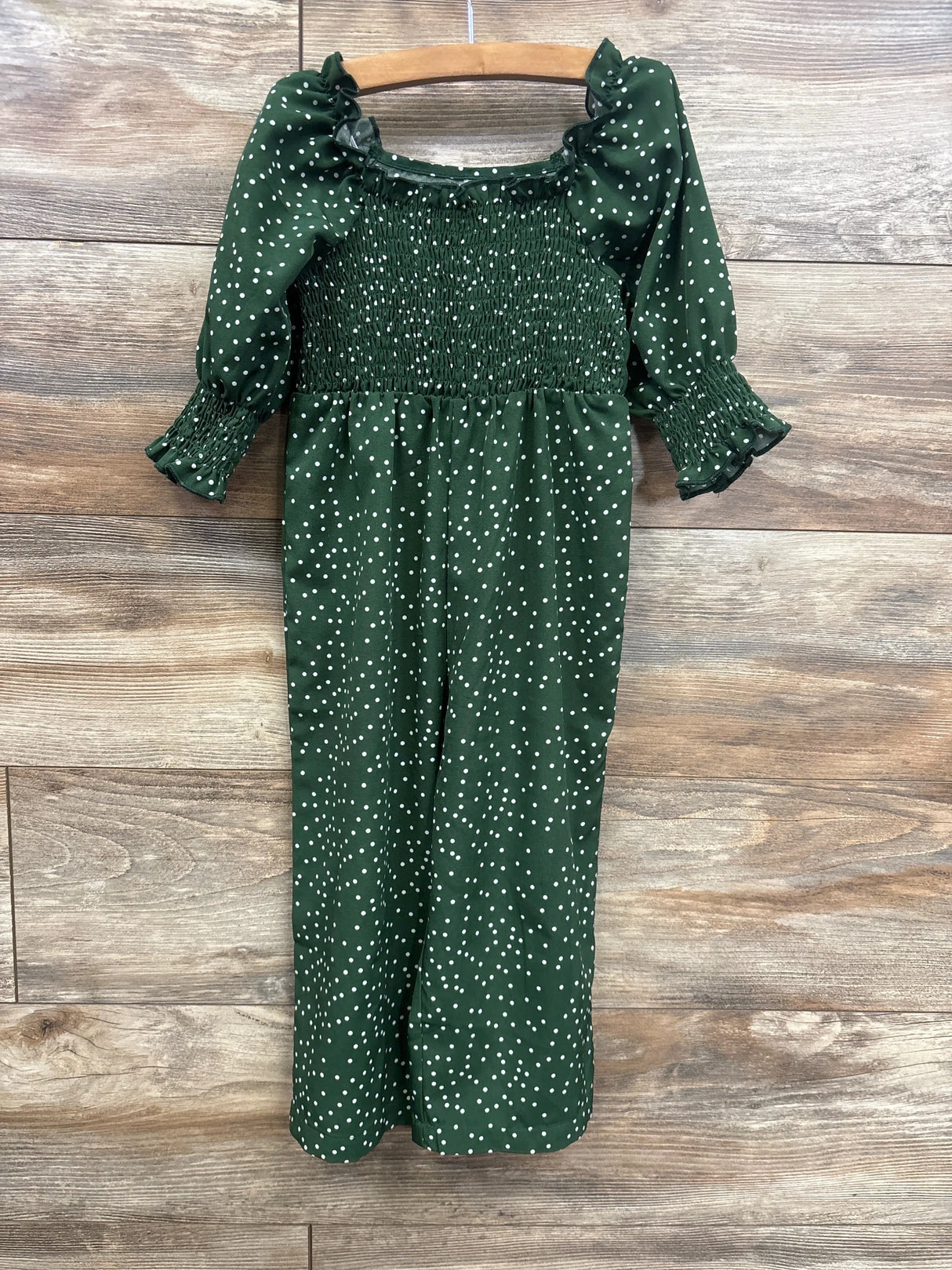 Front view of emerald polka dot smocked romper (2T) showing smocked bodice, ruffled sleeves on wooden hanger against wood background