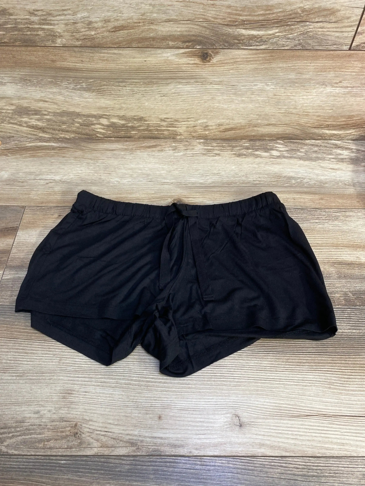 Flat lay of Gap maternity modal shorts in black showcasing elastic drawstring waistband and layered curved hem on wood floor