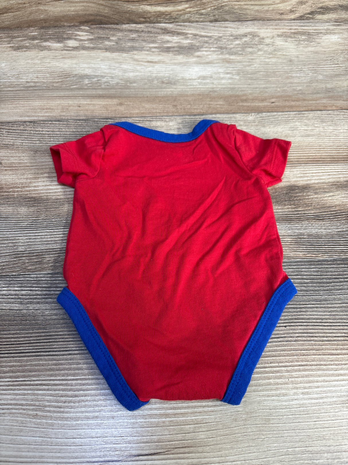 Red baby onesie with blue trim on a wooden background