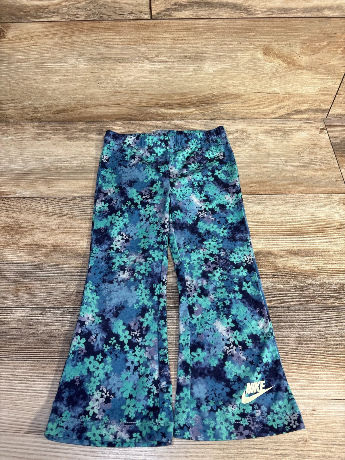 Front view of Nike Dri-Fit floral flared leggings showcasing blue floral print and Nike logo on wooden background