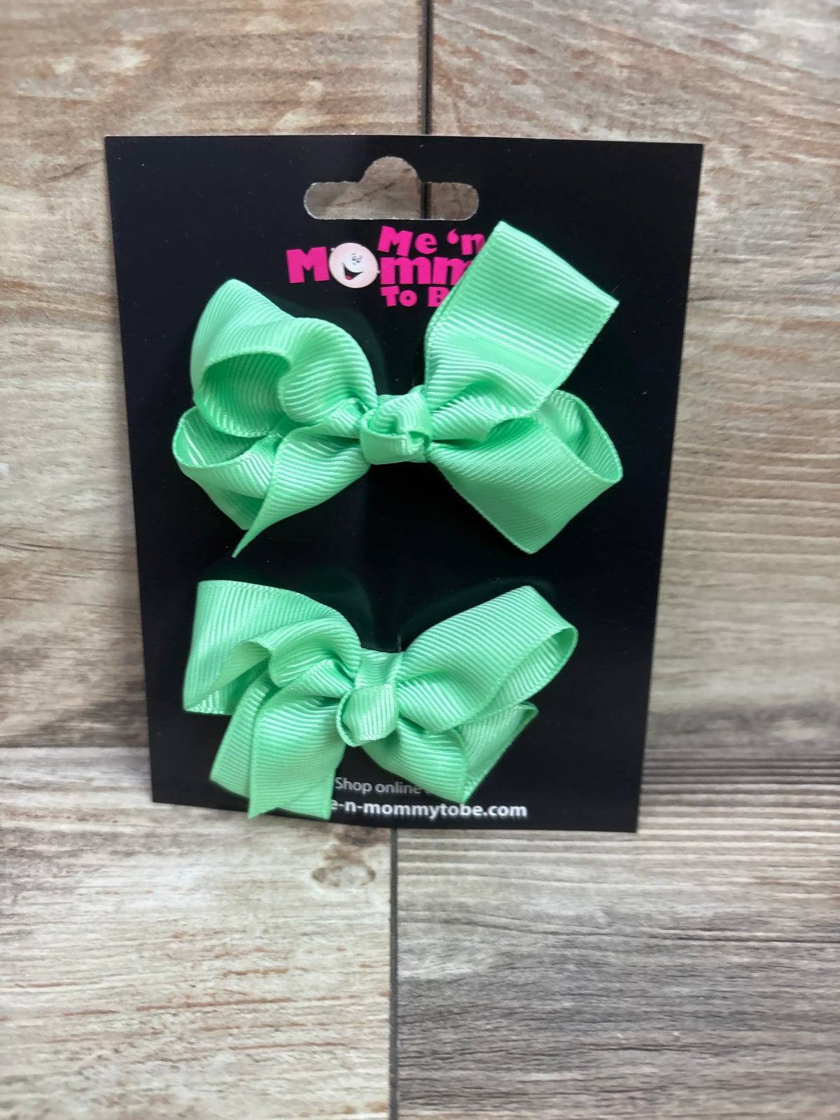 Two mint green grosgrain hair bows on a black Me n Mommy To Be display card.