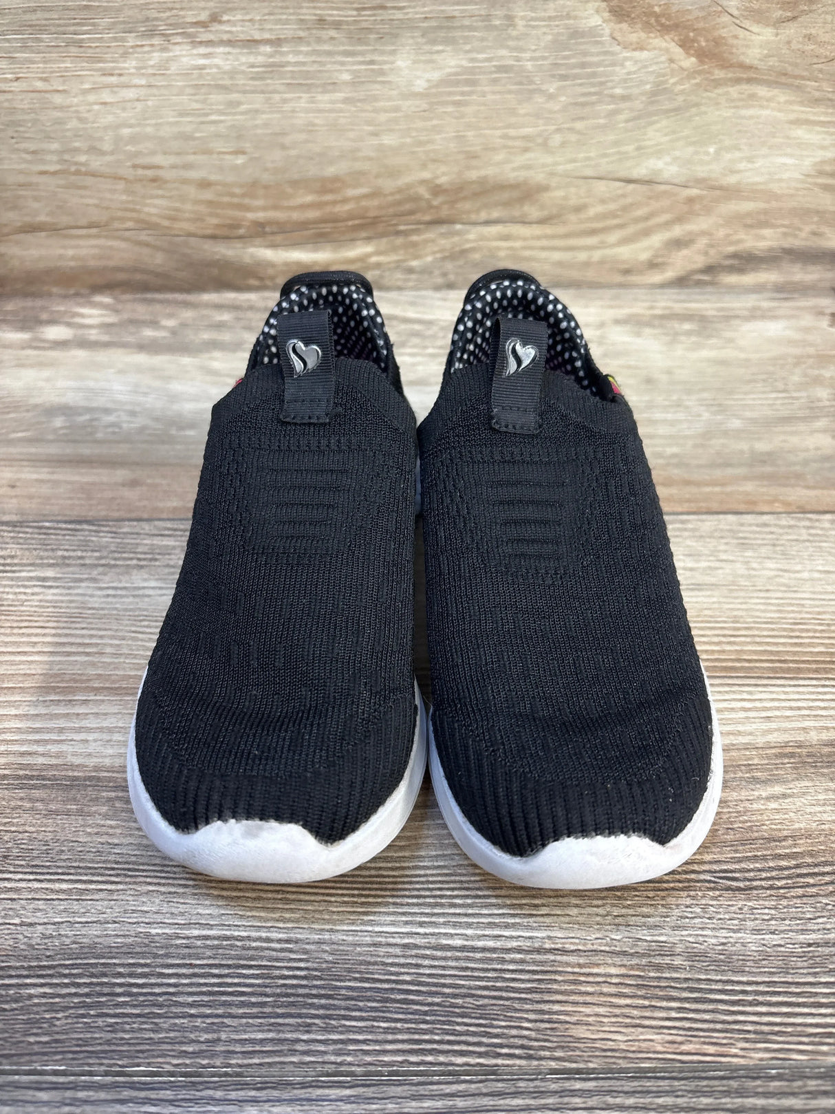 Black slip-on kids sneakers with white soles on wood background, gently used children's shoes