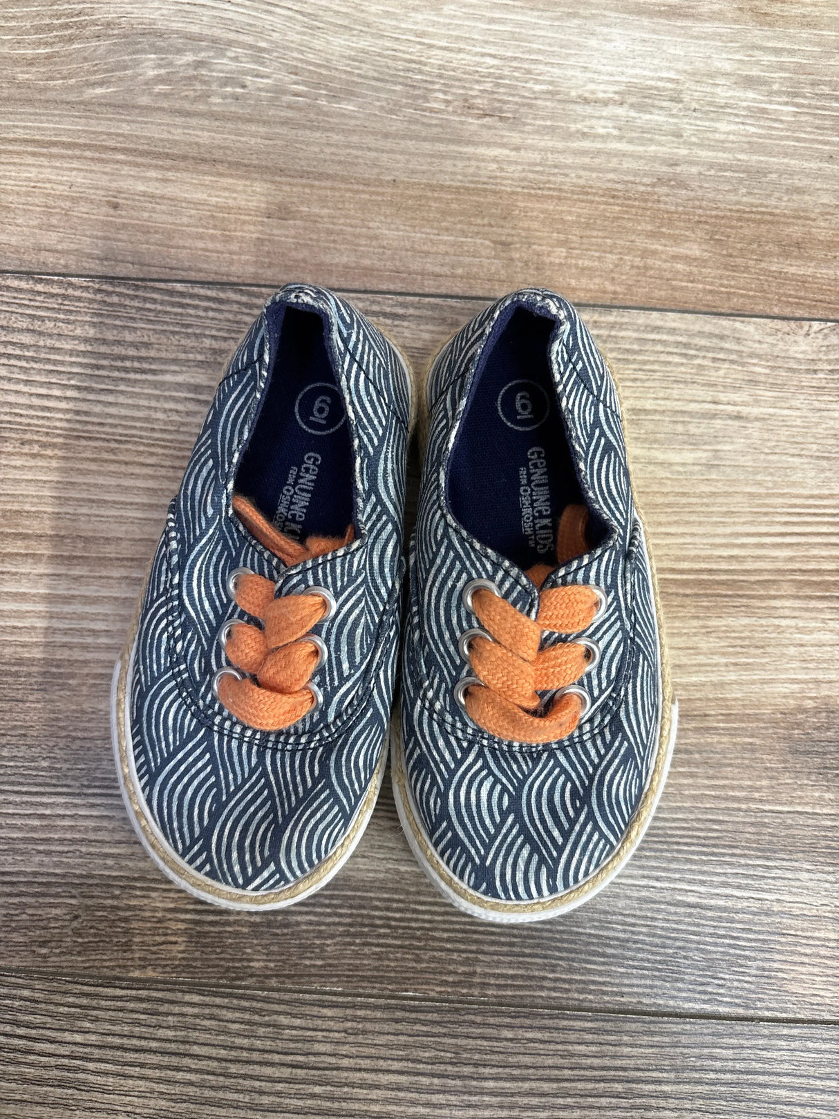 Top view of Genuine Kids OshKosh Tailynn Sneakers blue sz 6c showcasing wave print with orange laces on wood plank floor