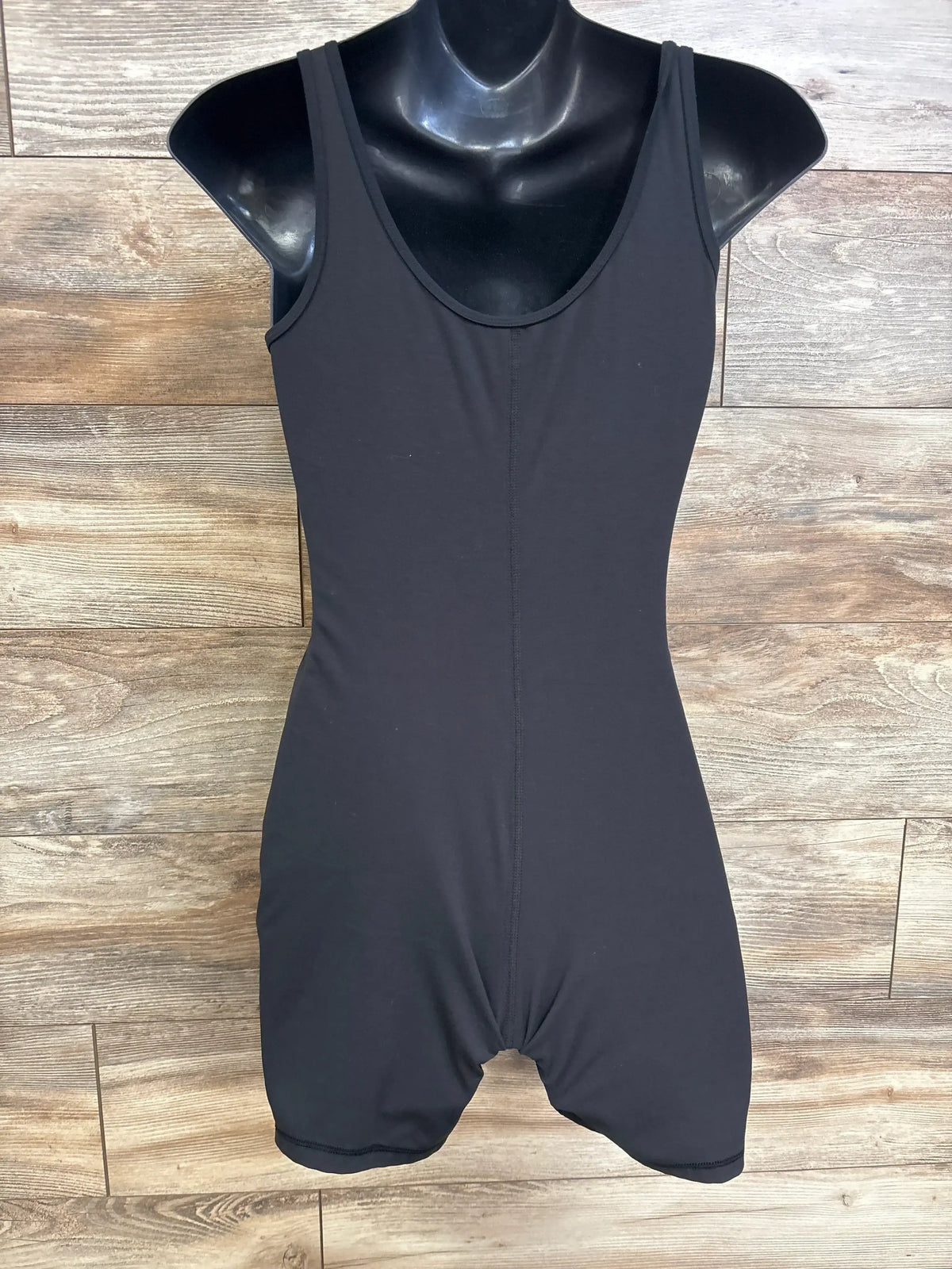 Front view of black Isabel maternity active romper showcasing a sleeveless scoop neckline and mid-thigh shorts with a wood background
