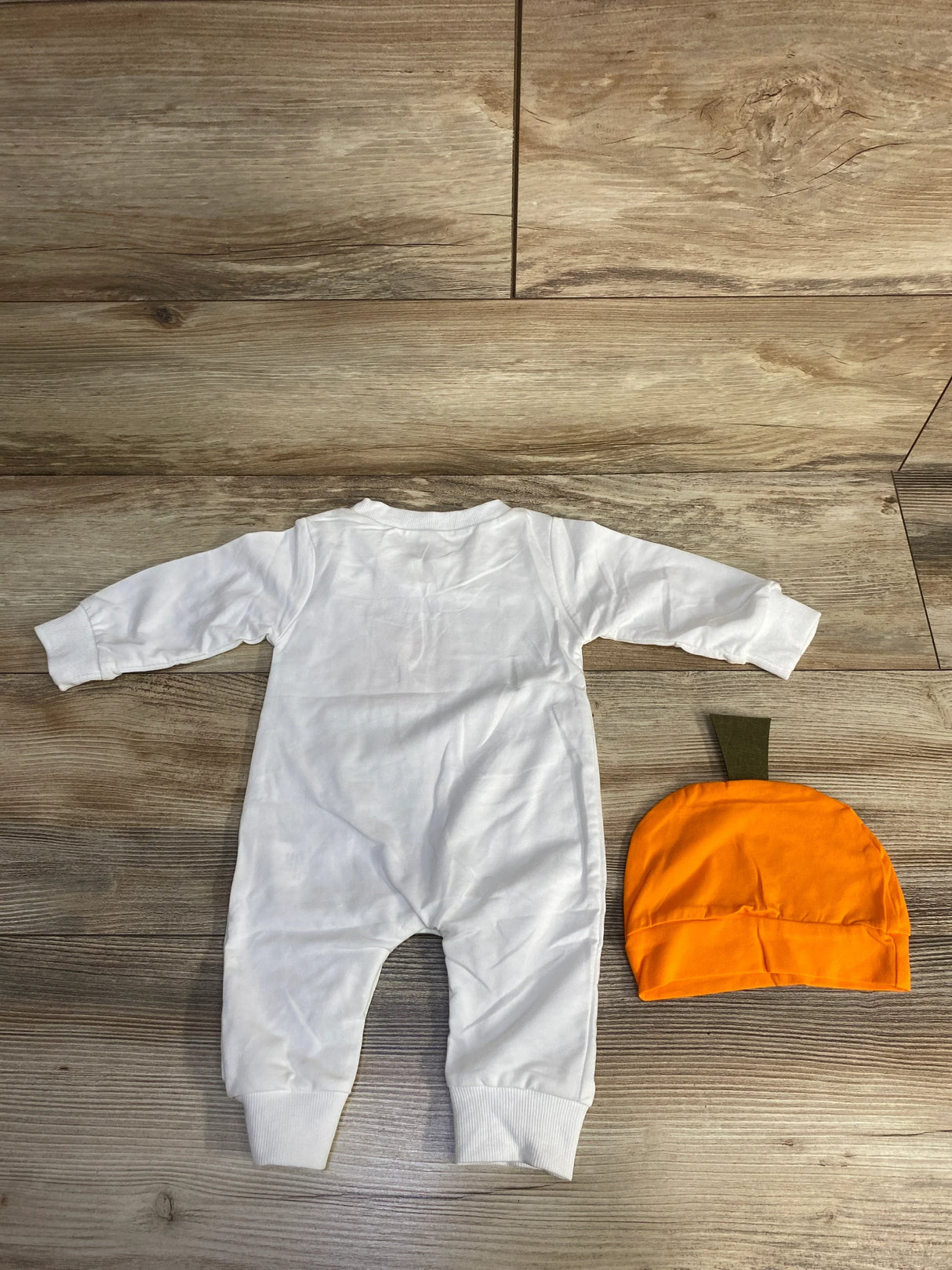 White baby onesie with orange pumpkin hat on wood floor, perfect for fall or Halloween outfits