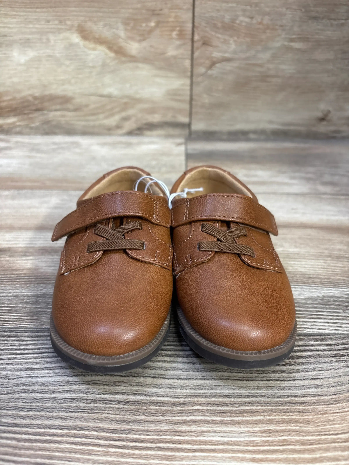 Front view of Cat and Jack Miles dress shoes in cognac with hook and loop straps and laces on a wood look floor