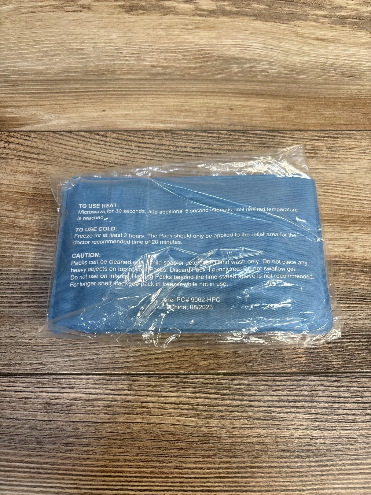 Reusable blue hot cold gel pack in plastic wrap on wooden surface, care instructions visible.