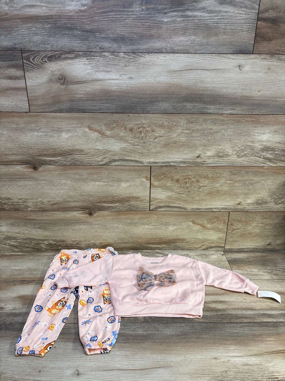 Flat lay of toddler Bluey two piece set pink bow sweatshirt and matching printed joggers on wood background