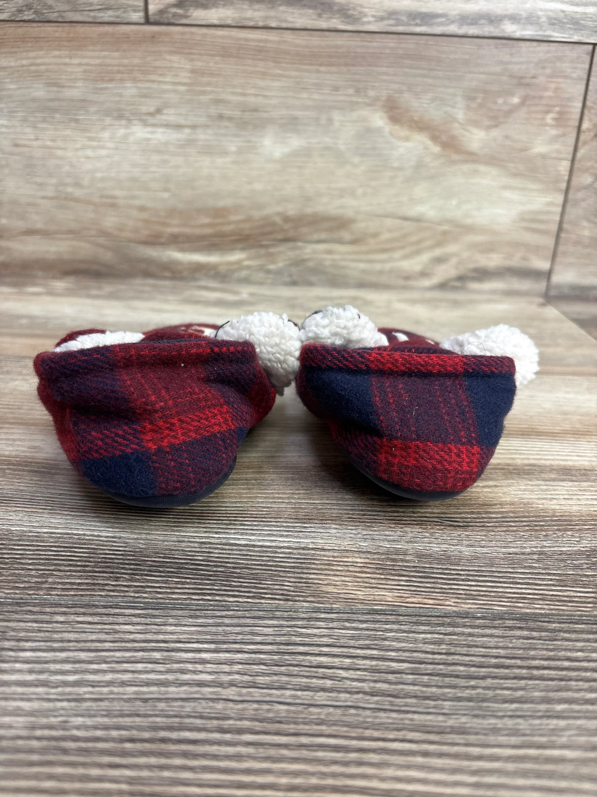 Red and navy plaid baby booties with white fuzzy lining on wood floor