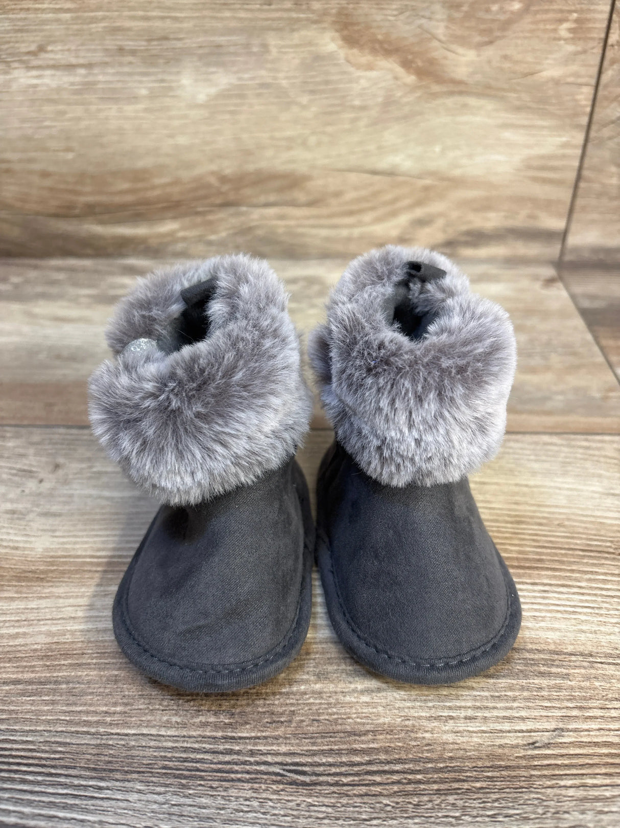 Front view of First Steps soft sole faux fur baby boots in gray, showing plush fur cuffs and soft sole on wooden background