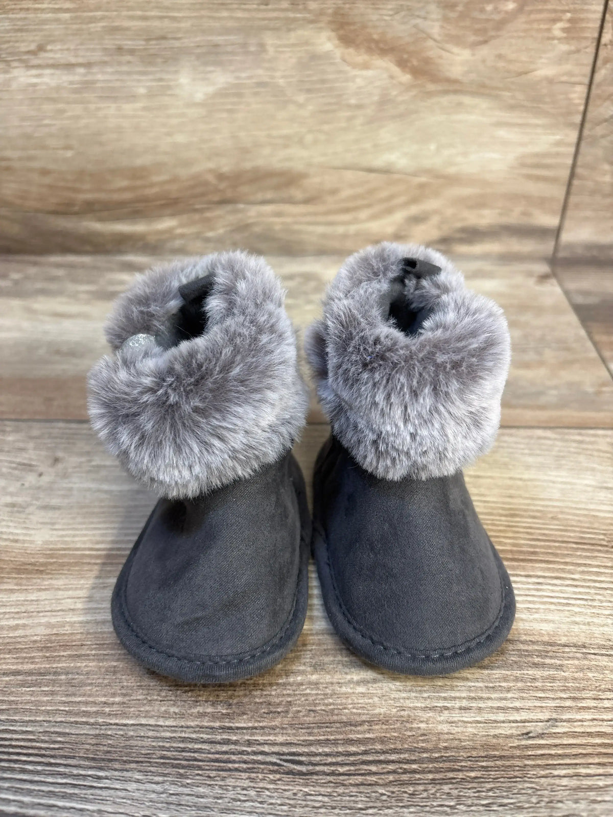 Front view of First Steps soft sole faux fur baby boots in gray, showing plush fur cuffs and soft sole on wooden background