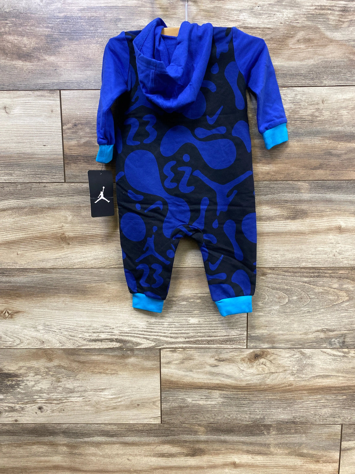 Blue and black baby onesie with hood and abstract pattern, displayed on wooden floor with Jordan brand tag