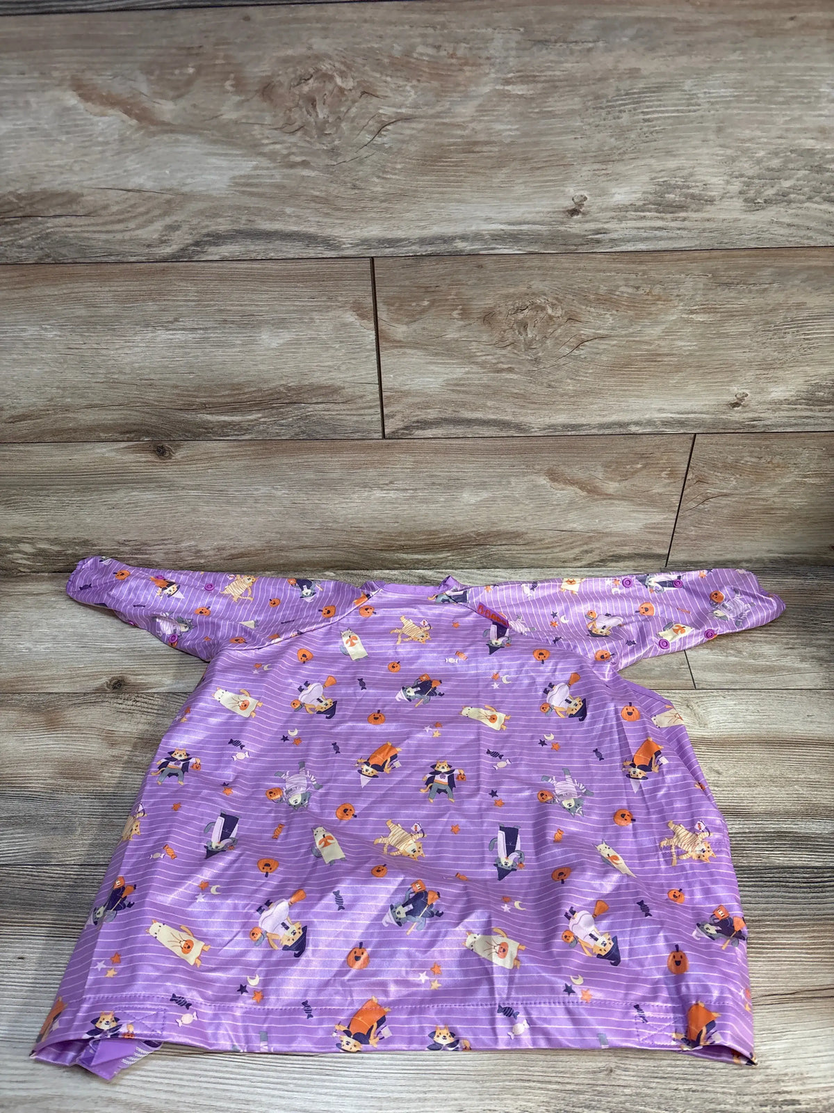 Front view of the Bibado Coverall Weaning Bib in Animal Halloween Purple showcasing long sleeves and full coverage on a wood-look floor