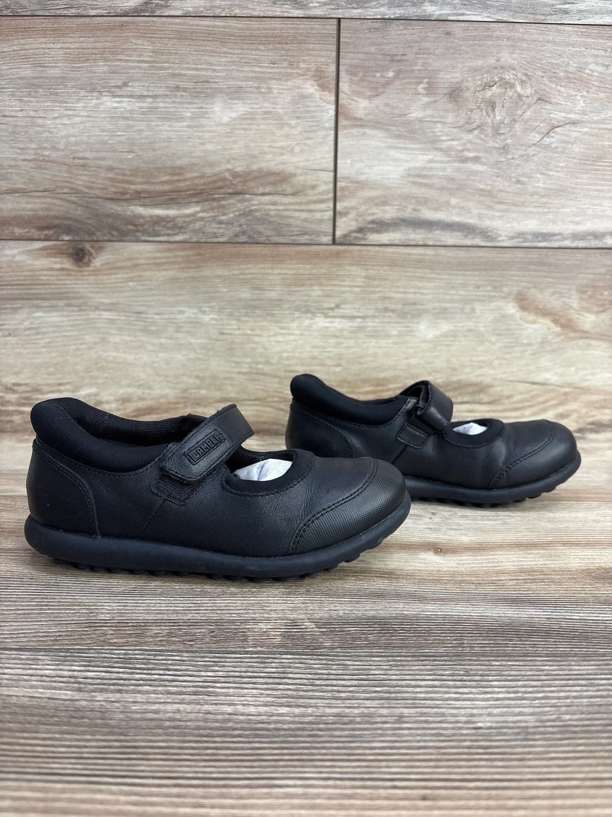 Black Mary Jane kids shoes with Velcro straps on wood floor, gently used children's footwear