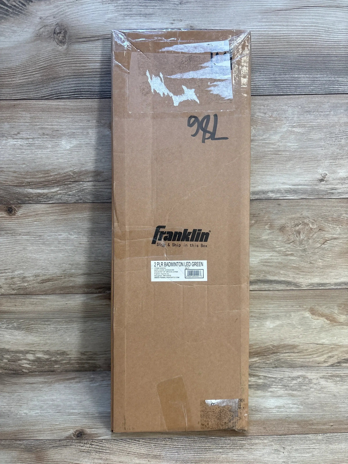 Top-down view of boxed Franklin Sports two-player LED badminton racket set showing Franklin logo and factory label on wooden floor