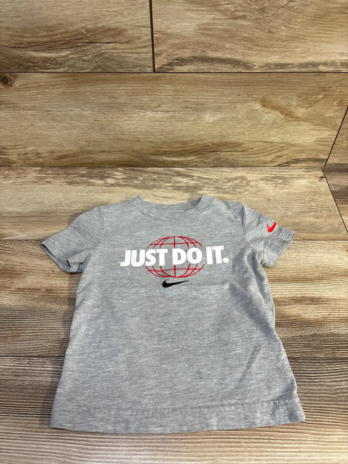 Front view of grey toddler Nike tee 2T showing JUST DO IT. over red globe and black swoosh on wood floor