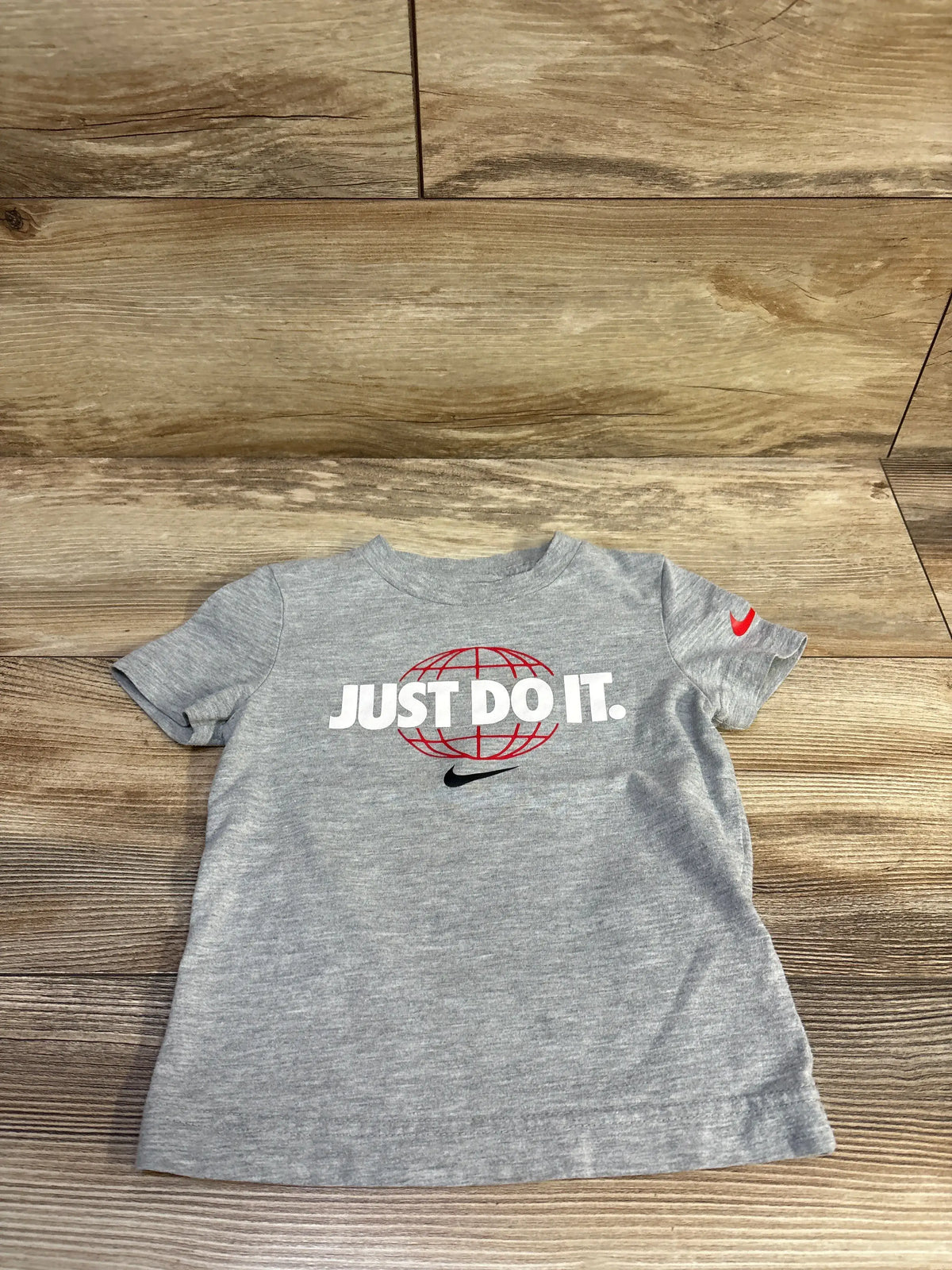Front view of grey toddler Nike tee 2T showing JUST DO IT. over red globe and black swoosh on wood floor