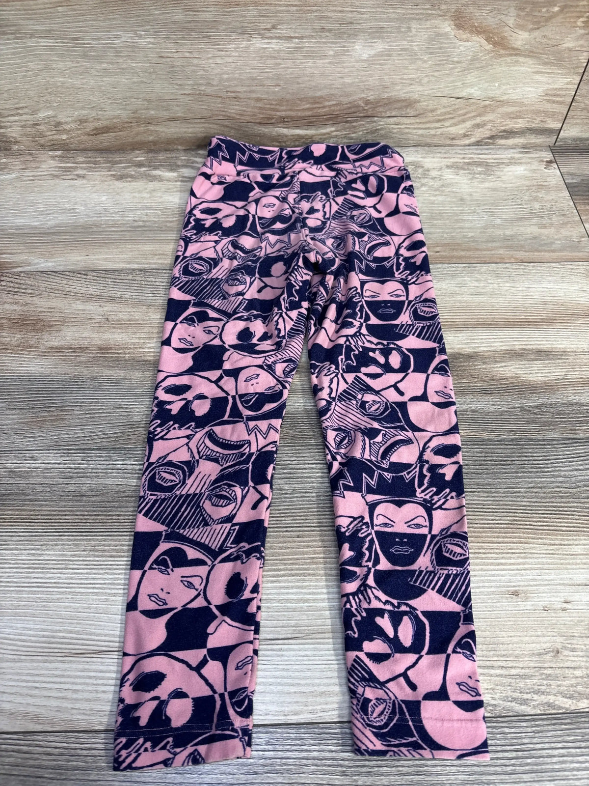Flat lay of pink Lularoe Evil Queen toddler leggings showing navy villain face print and elastic waist on wood background