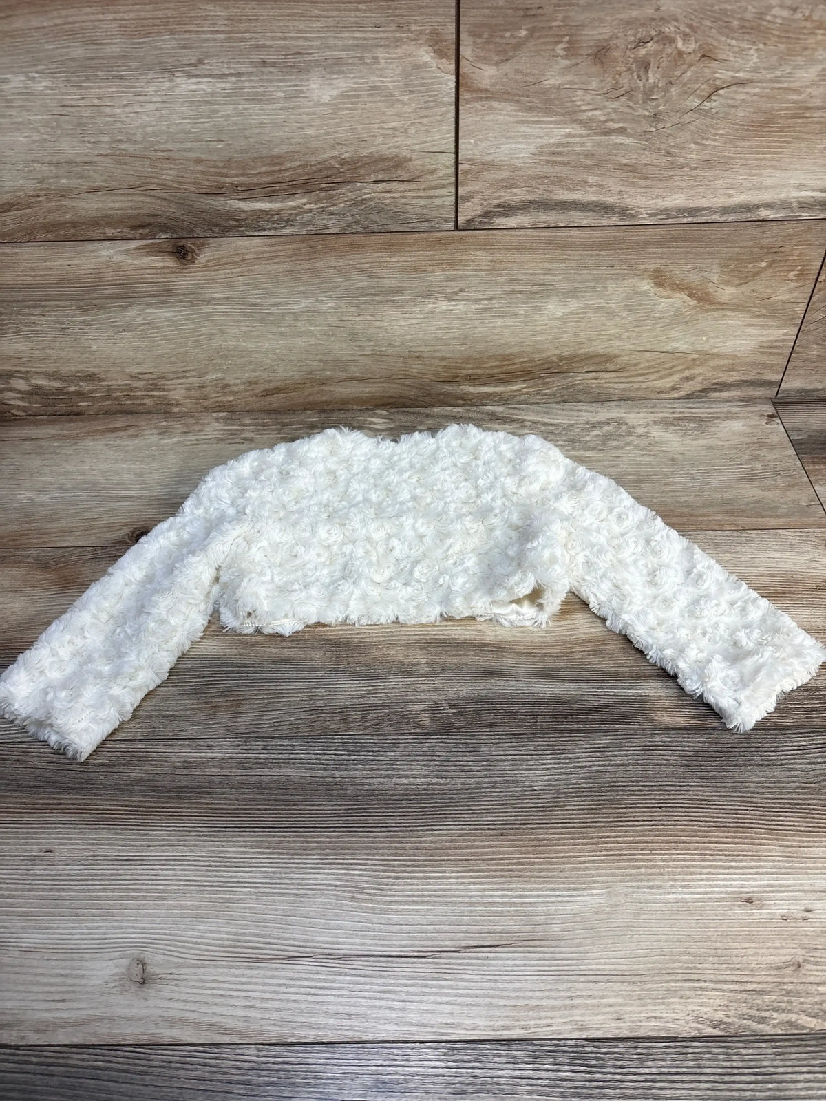 White textured baby bolero jacket with long sleeves on wooden background