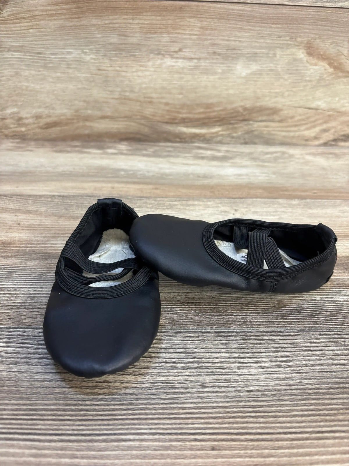 Black toddler ballet shoes with elastic straps on a wooden surface