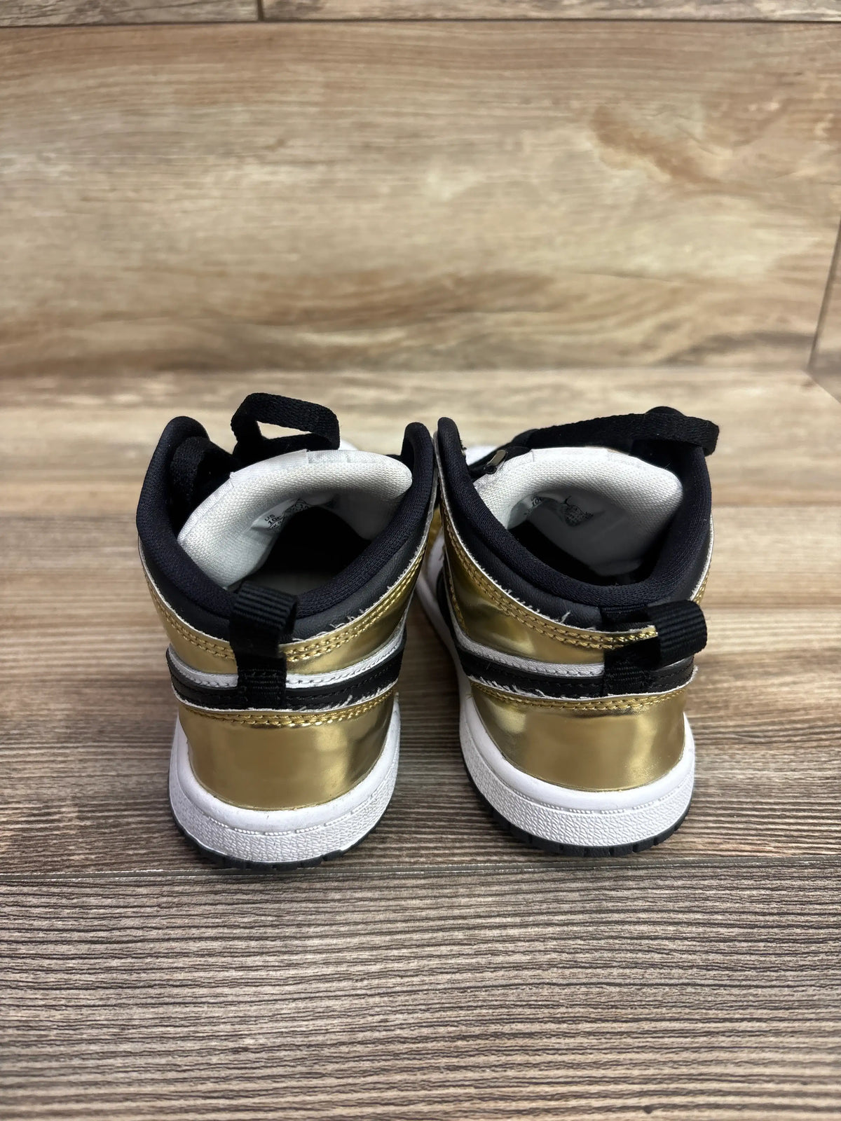 Rear view of Air Jordan 1 Mid SE TD sneakers, size 10C, showcasing metallic gold panels and white soles on a wood floor