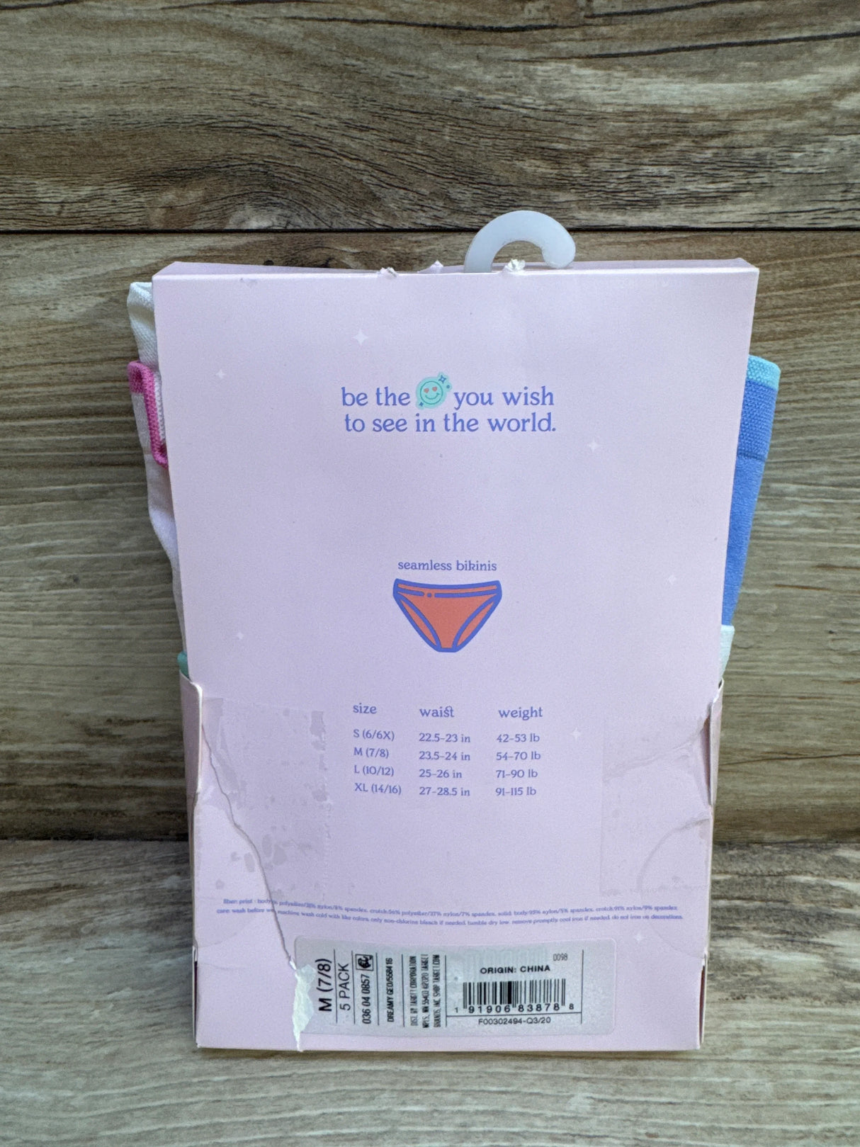 Rear view of 5-pack seamless bikinis packaging showing size M 7/8 sticker, size chart, and pink box against wood background