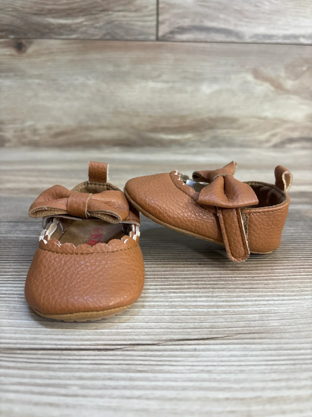 Brown leather baby shoes with bows on wooden background