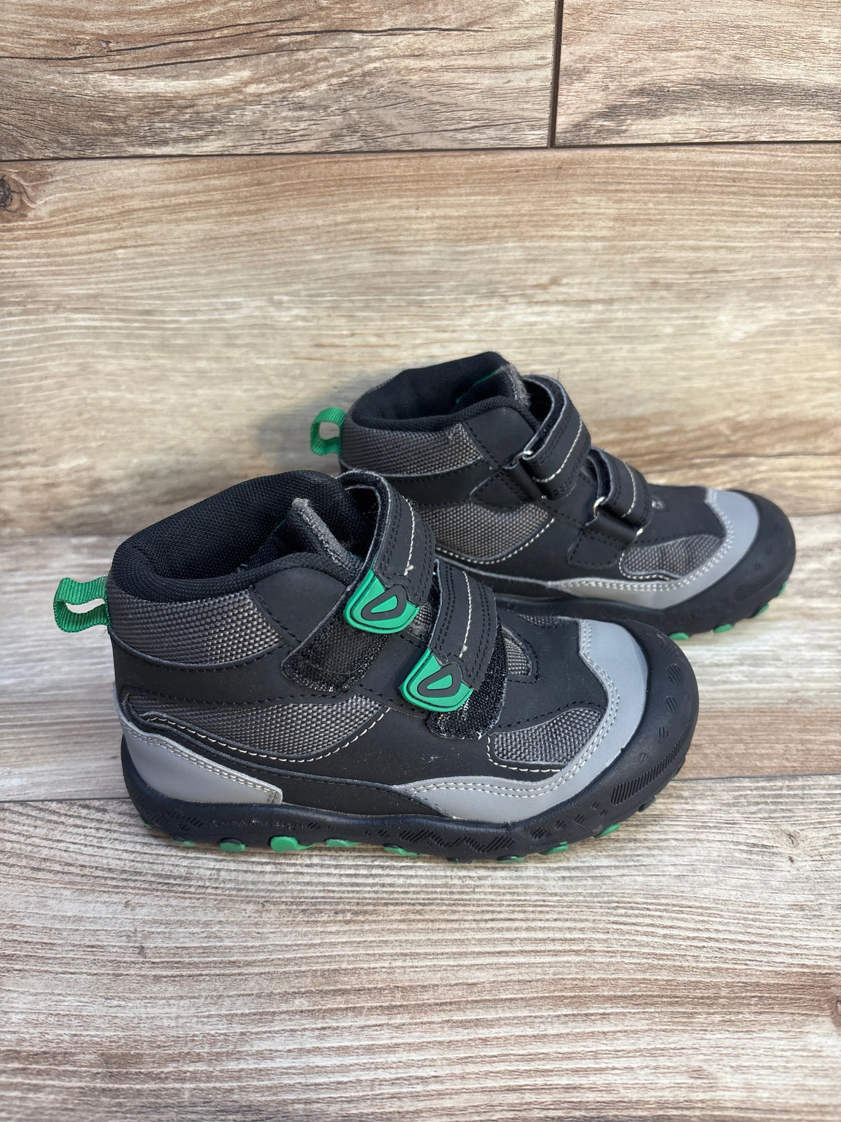 Kids’ black and gray hiking boots with green accents on wood floor