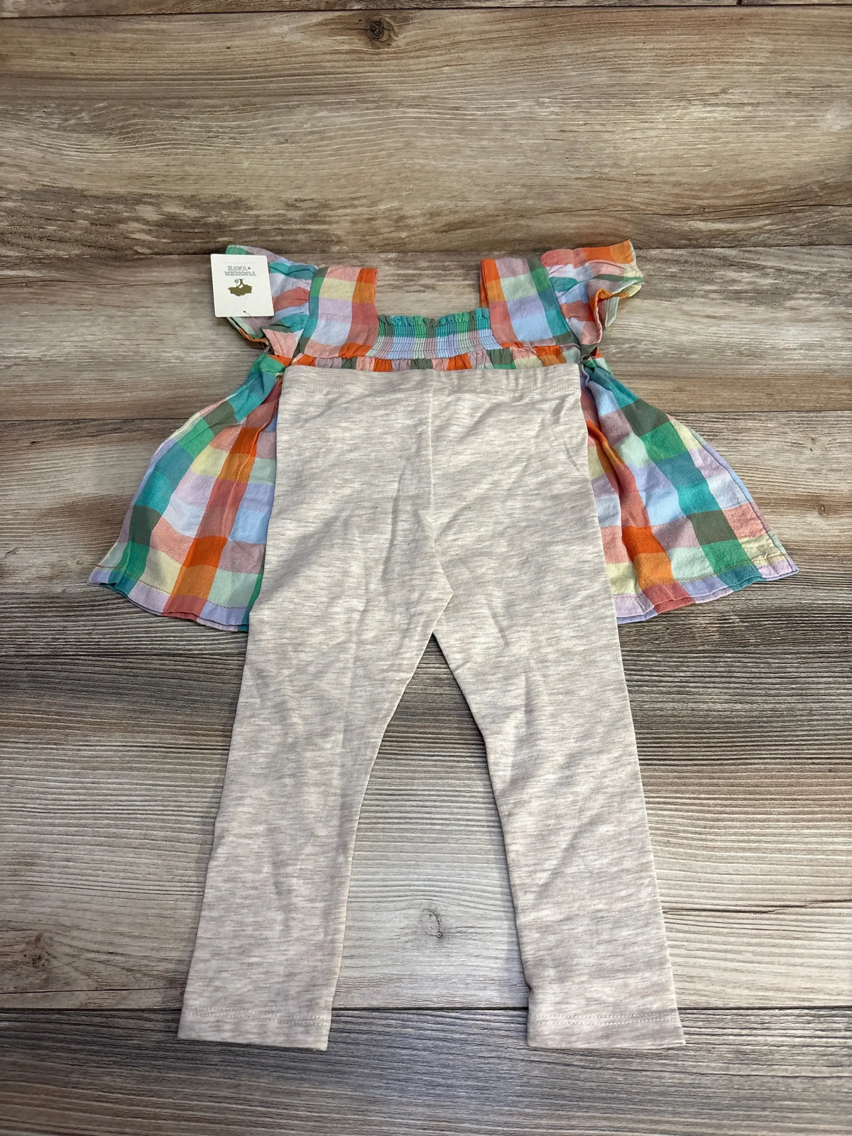 Flat lay of Tucker + Tate 2-piece top and leggings showing multicolor checked flutter-sleeve top and heather leggings on wood