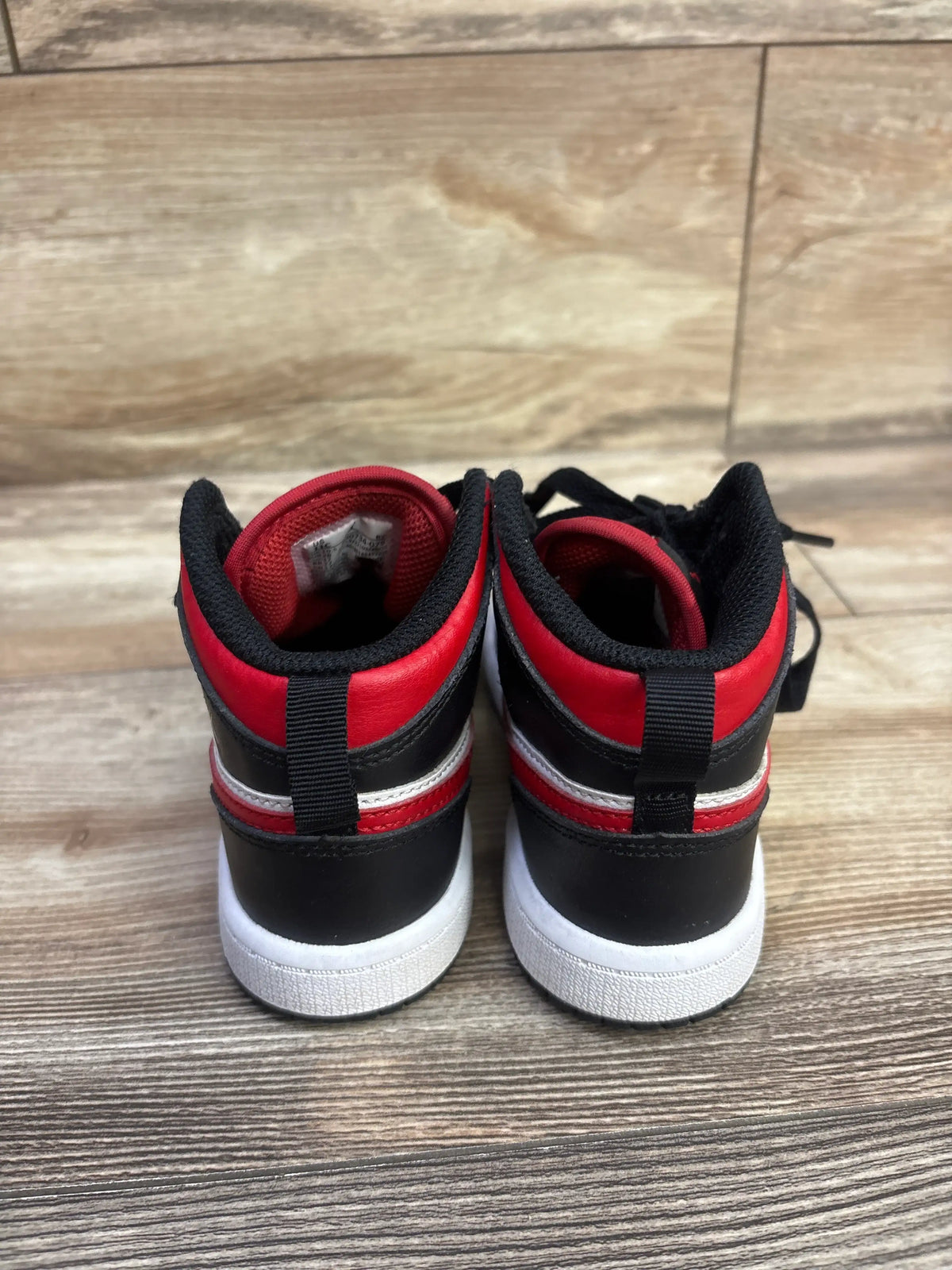 Rear view of Air Jordan 7 Retro TD Citrus sneakers showcasing red, black, and white high-top design on wood-look flooring