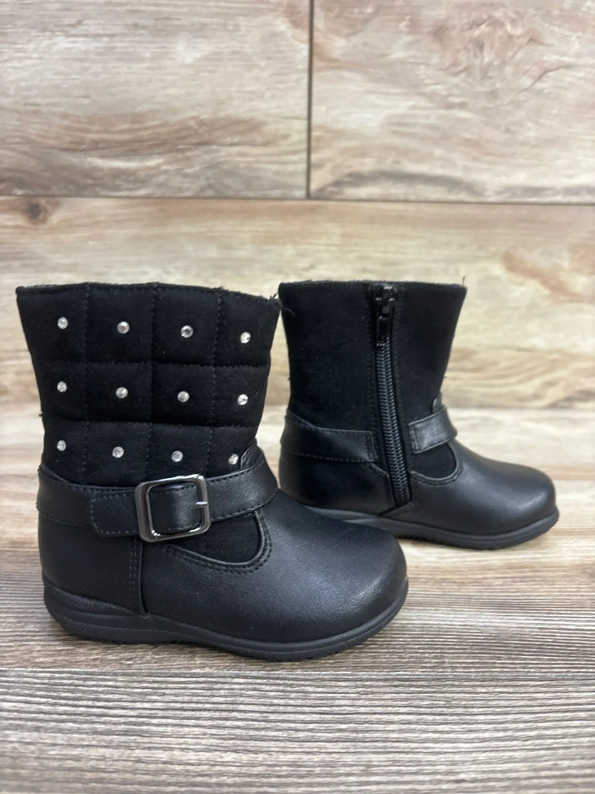 Pair of black toddler boots with studded quilted upper and side zipper on wooden floor