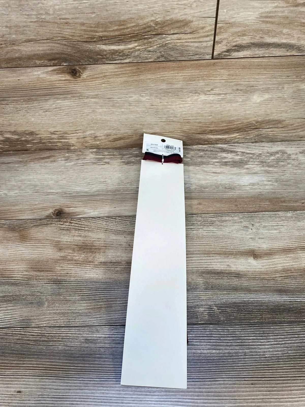 Top-down view of Cat & Jack adjustable zip necktie in wine showing zip-adjuster and retail tag on light wood floor