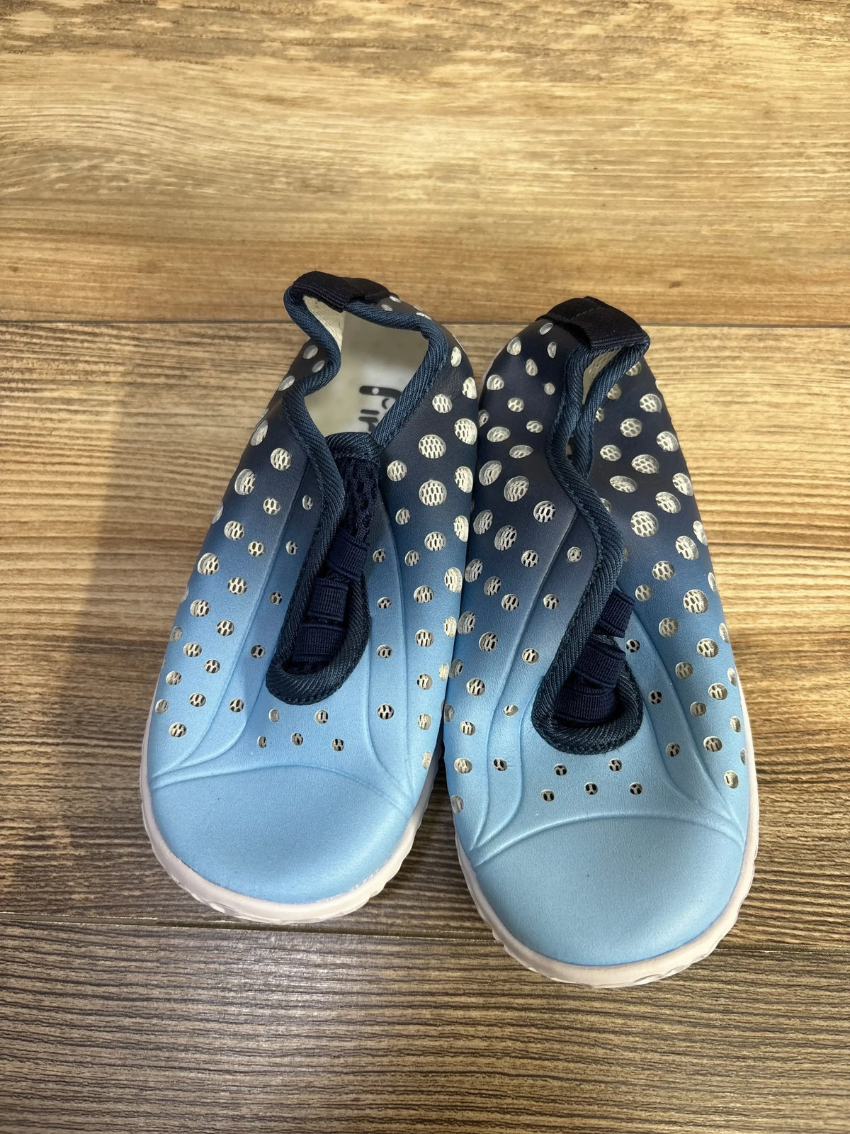 Top view of blue Fires Barefoot quick-dry toddler water shoes showcasing perforated upper, elastic gore, and white sole on wood floor