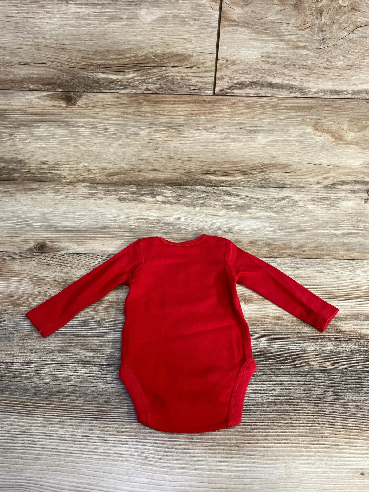 Flat lay of red long-sleeve Wee Play baby bodysuit (0-3 months) showing the back and snap-closure crotch on a wood floor background