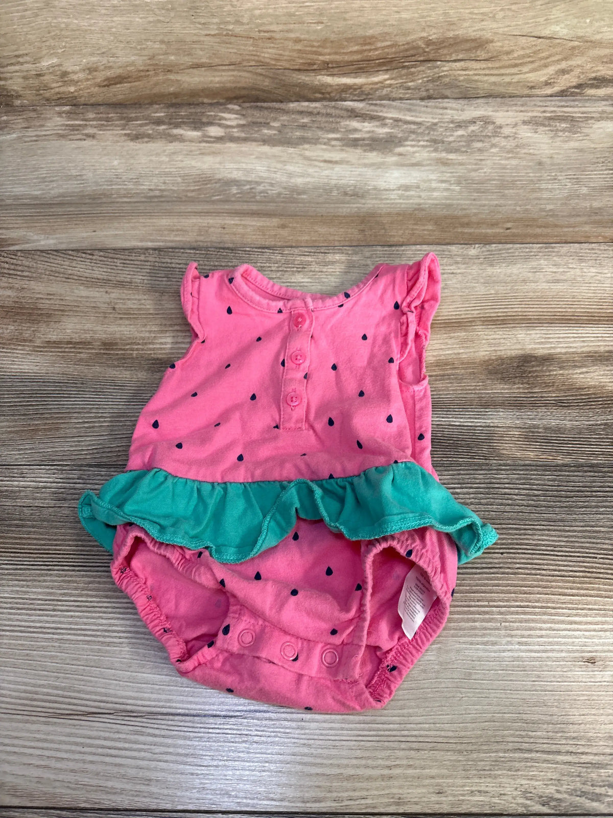 Front view of Carter’s pink watermelon bubble romper showcasing green ruffle and snap closure on wood background
