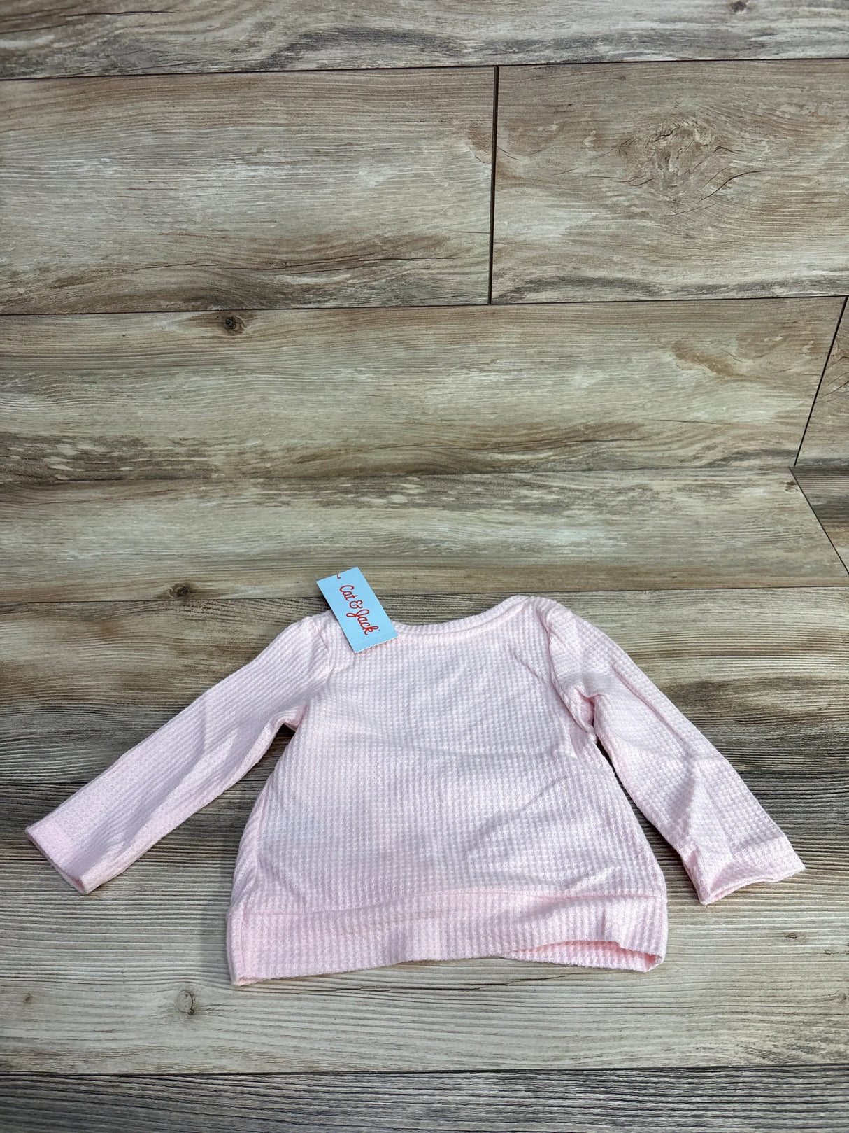 Light pink long sleeve baby shirt with textured fabric and tag on wood floor background