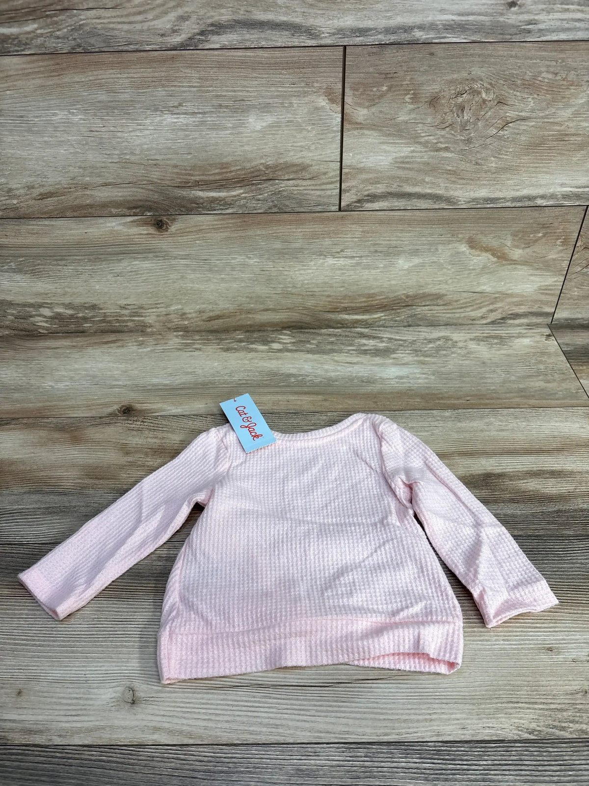 Light pink long sleeve baby shirt with textured fabric and tag on wood floor background